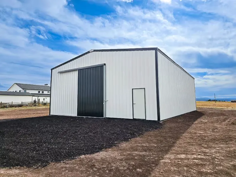 Completed Mammoth metal building — white steel with charcoal trim and a sliding door on a rural site